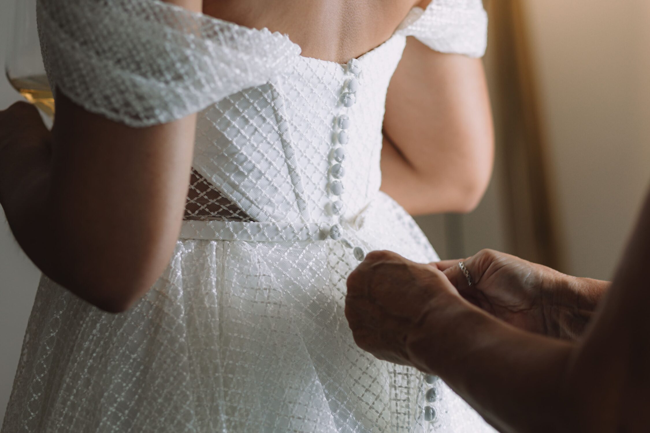 Noiva de costas, apertando vestido de noiva branco, para casamento em Santorini, Grécia