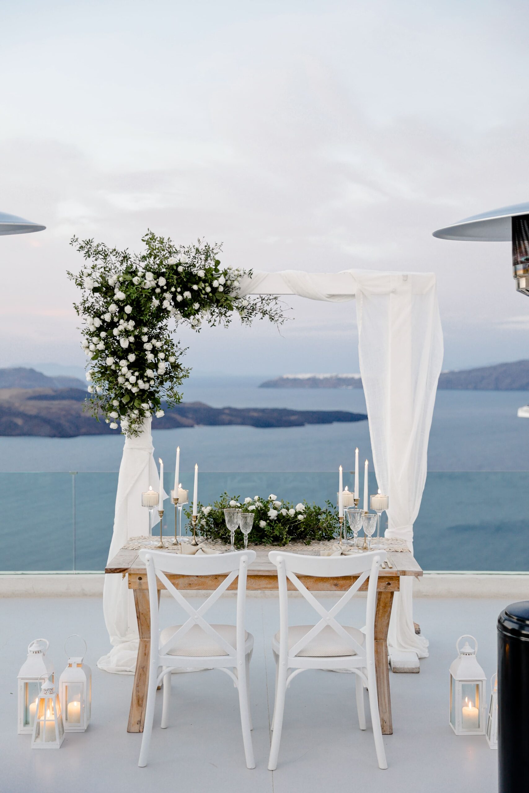 Gazebo decorado com arranjo, e mesa posta para jantar com velas e itens florais, em Santorini, Grecia