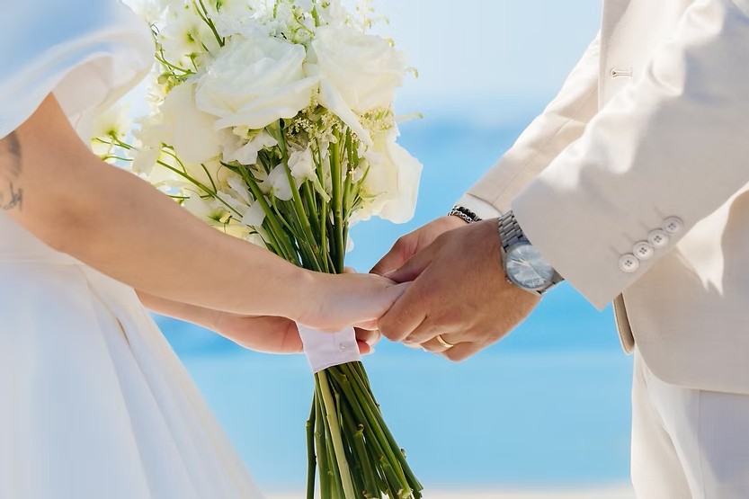 Casal de maos dadas, com um buque de flores nas maos, em Santorini, Grecia
