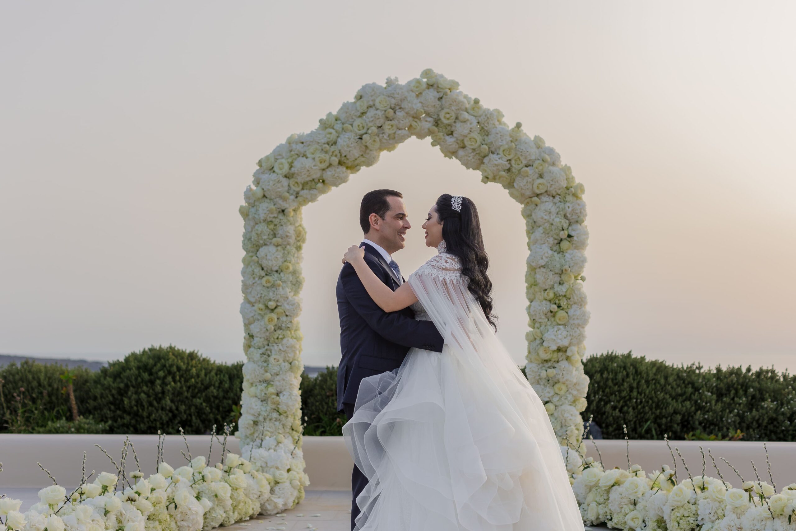 Casal se olhando em frente ao arco de flores em Santorini, Grecia